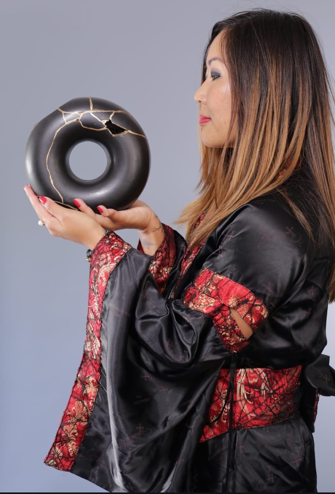 Thuy Gattaux présentant une œuvre kintsugi circulaire noire et dorée.