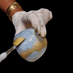 Main d’artiste appliquant de la poudre d’or sur une céramique restaurée selon la méthode du kintsugi.